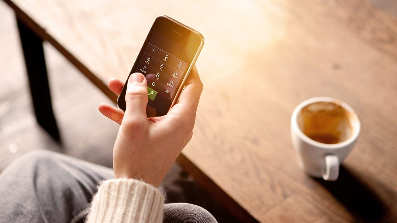 رجل يحمل هاتفًا نقالًا ويحتسي قهوة