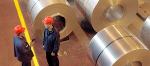 Two factory workers talking next to large rolls of steel