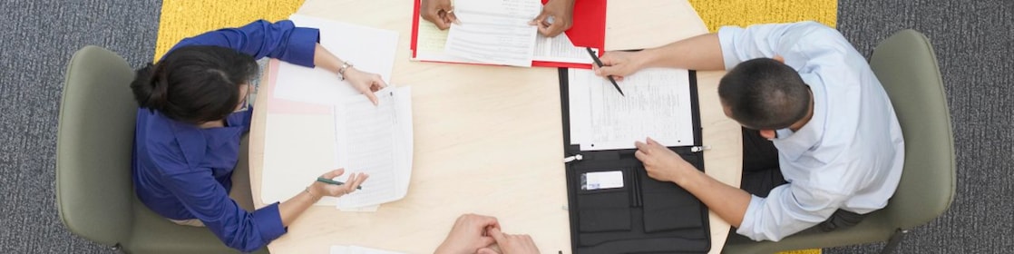 Four business people sitting around a round table reading documents, grey and yellow carpet